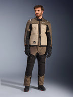 Alpinestars Cusco Drystar® Jacket in Walnut Aluminum Black, worn by a male rider with matching adventure touring pants, black gloves, and boots, featuring tan chest panels, black sleeves with subtle orange accents, and functional ventilation zippers for motorcycle road riding.