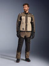 Alpinestars Cusco Drystar® Jacket in Walnut Aluminum Black, worn by a male rider with matching adventure touring pants, black gloves, and boots, featuring tan chest panels, black sleeves with subtle orange accents, and functional ventilation zippers for motorcycle road riding.