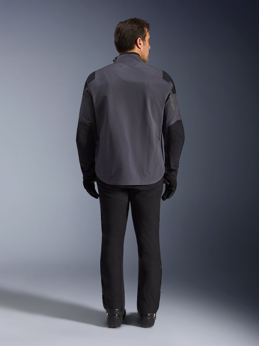 Alpinestars Maxdura Drystar®XF Laminated Armored Shell, Motorcycle Jacket, Deep Gray and Black, back view of a rider wearing full adventure gear, technical laminated shell with black reinforced shoulder and elbow panels, paired with black pants and gloves.