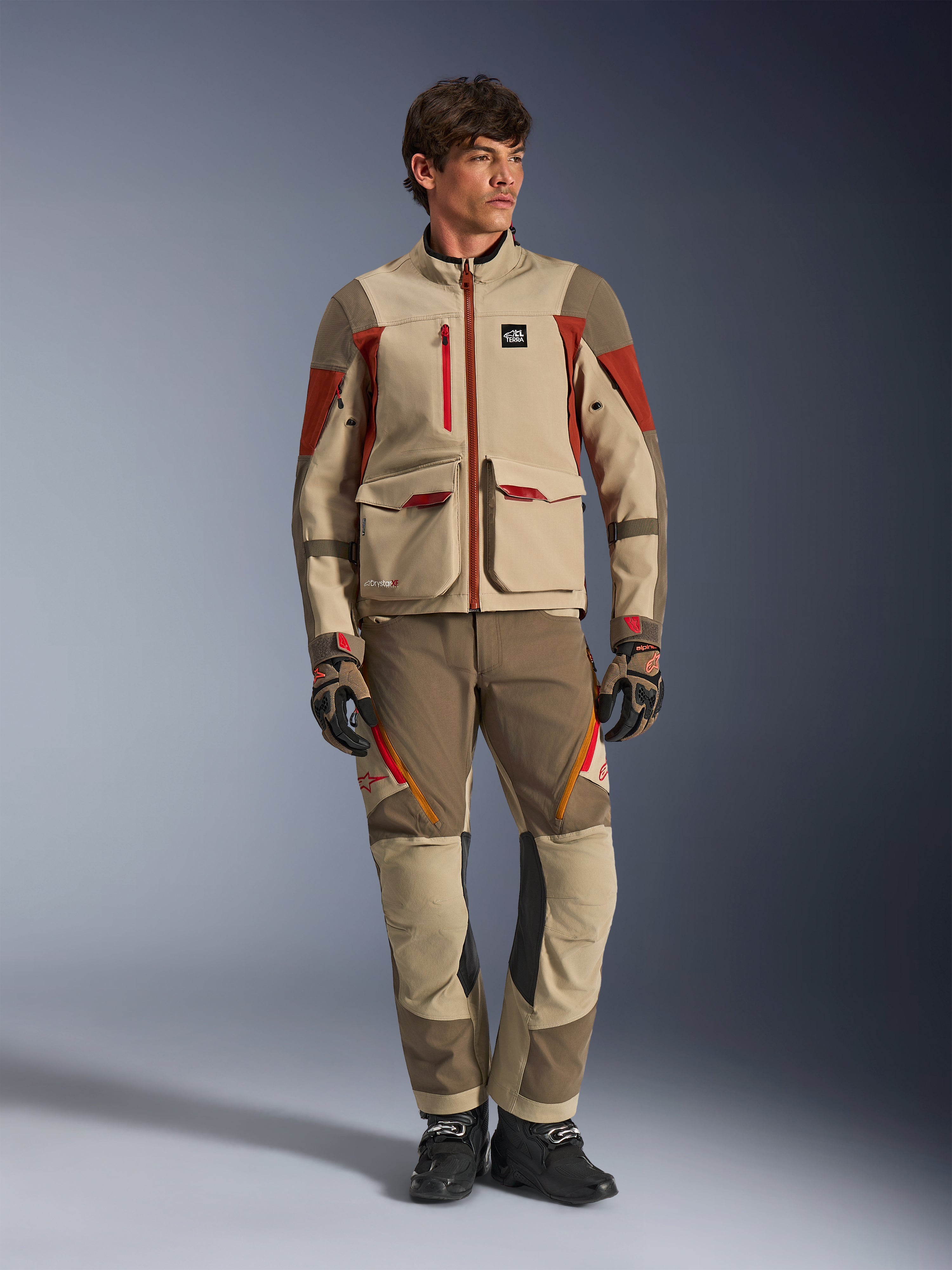 Maxdura Drystar®XF Laminated Armored Shell, adventure motorcycle jacket in Aluminum Walnut Rust Brown, worn by a male model with matching adventure pants, gloves, and boots, full-body studio shot of professional touring gear.