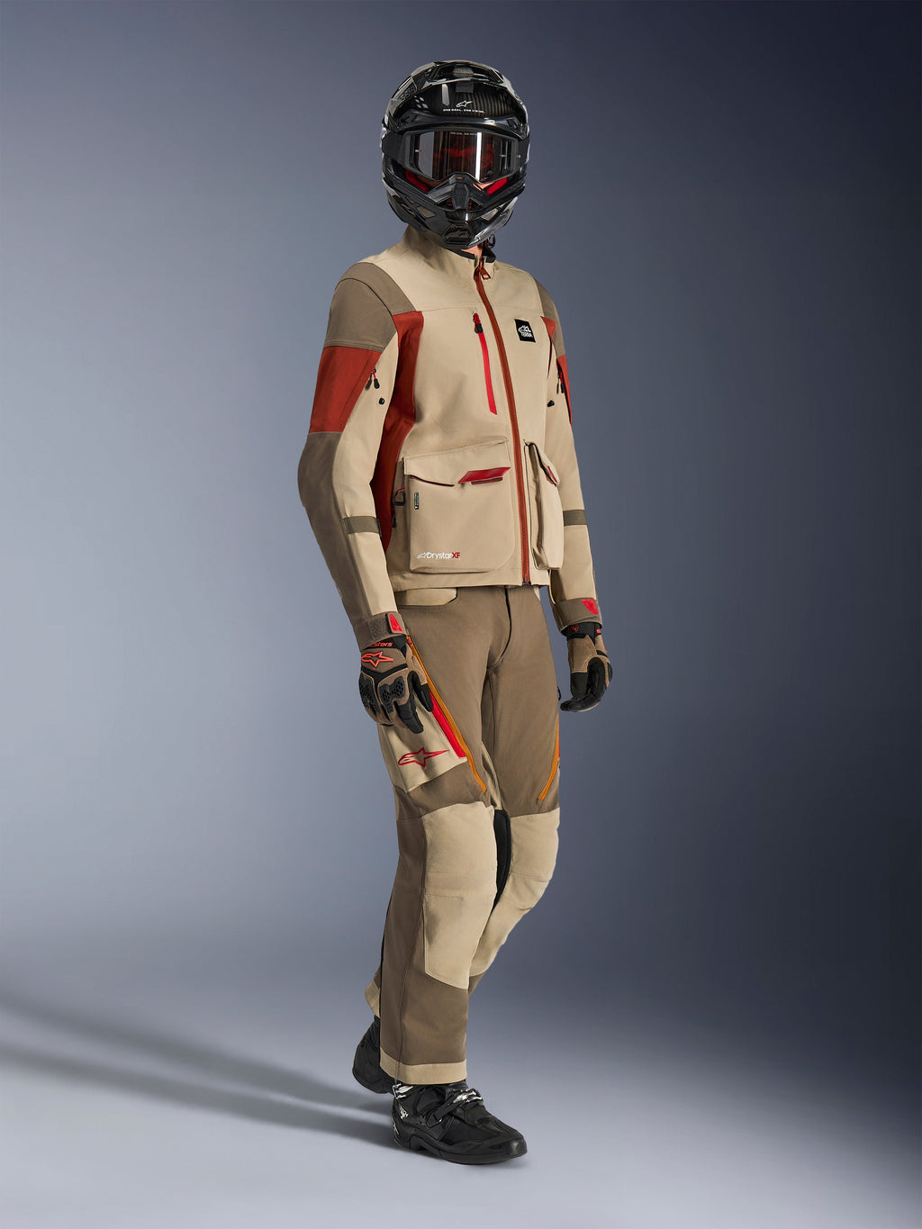 Adventure rider wearing Maxdura Drystar®XF Laminated Armored Shell, Aluminum Walnut and Rust Brown jacket with matching walnut and tan pants, black carbon fiber helmet, and black motorcycle boots, technical touring gear for adventure motorcycling