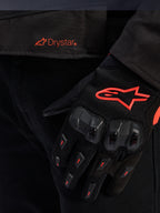 Close-up of the Alpinestars T-GP R V3 Drystar® Jacket waist featuring a red Drystar logo, shown with a black motorcycle glove with a red Alpinestars star logo, mesh fabric, and reinforced knuckle protection.