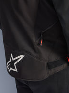Alpinestars T-GP R V3 Drystar® Jacket, Black and White, close-up view of the lower back section featuring a large white Alpinestars star logo, a side zippered pocket with a red pull tab, and a velcro waist adjustment strap, durable textile material.