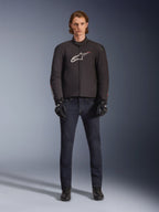 Model wearing Alpinestars SMX Waterproof Jacket in Black with white and red logo, paired with dark denim riding pants, black gloves, and riding boots, sporty all-weather motorcycle gear outfit.