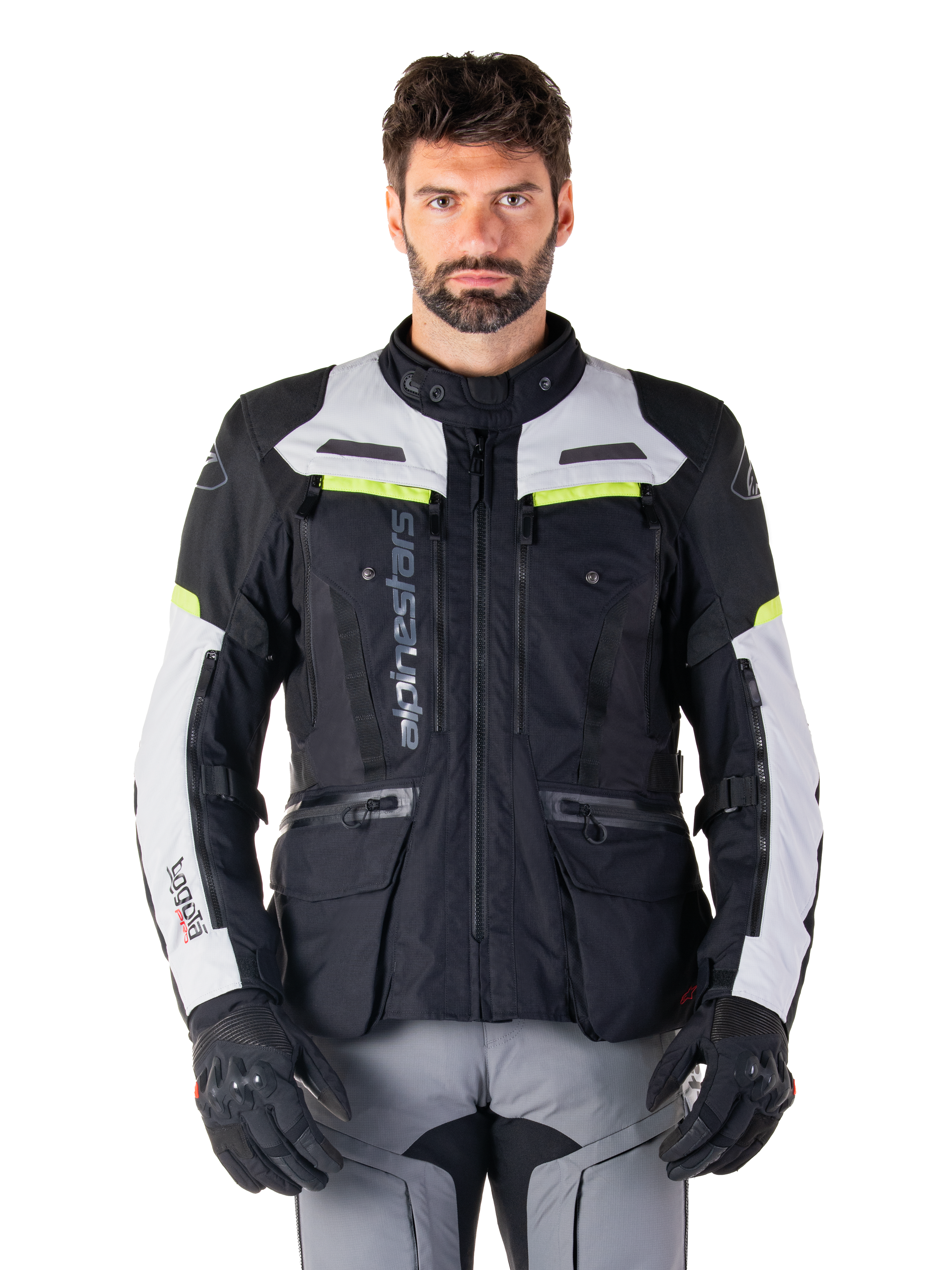 Man wearing Alpinestars Bogotá Pro Drystar® Jacket, Black Ice Gray and Yellow Fluo, all-season adventure touring motorcycle jacket, waterproof design with multiple pockets and vertical branding, paired with black gloves and gray riding pants