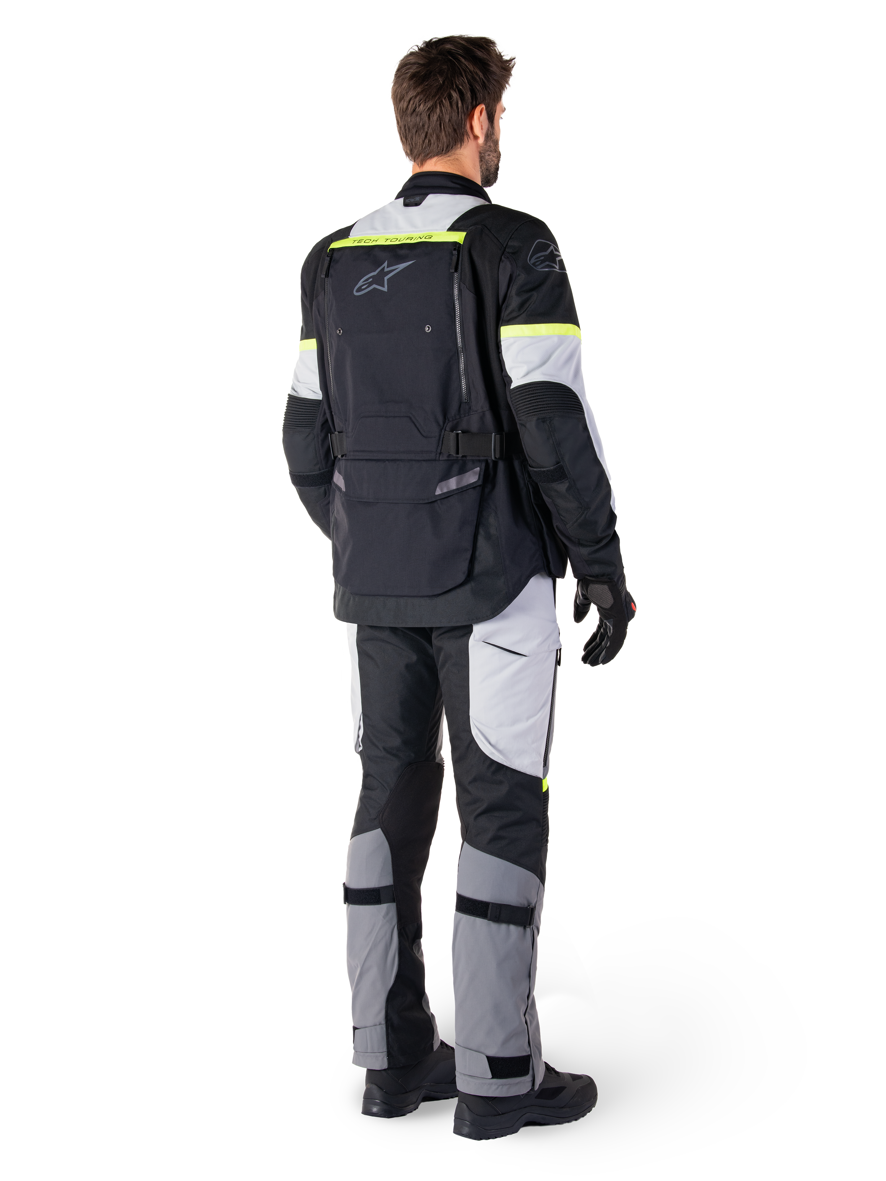 Rear view of a rider wearing the Alpinestars Bogotá Pro Drystar® Jacket in Black Ice Gray Yellow Fluo, paired with matching adventure touring pants, featuring a large back pocket and yellow fluorescent accents, all-season textile motorcycle gear.