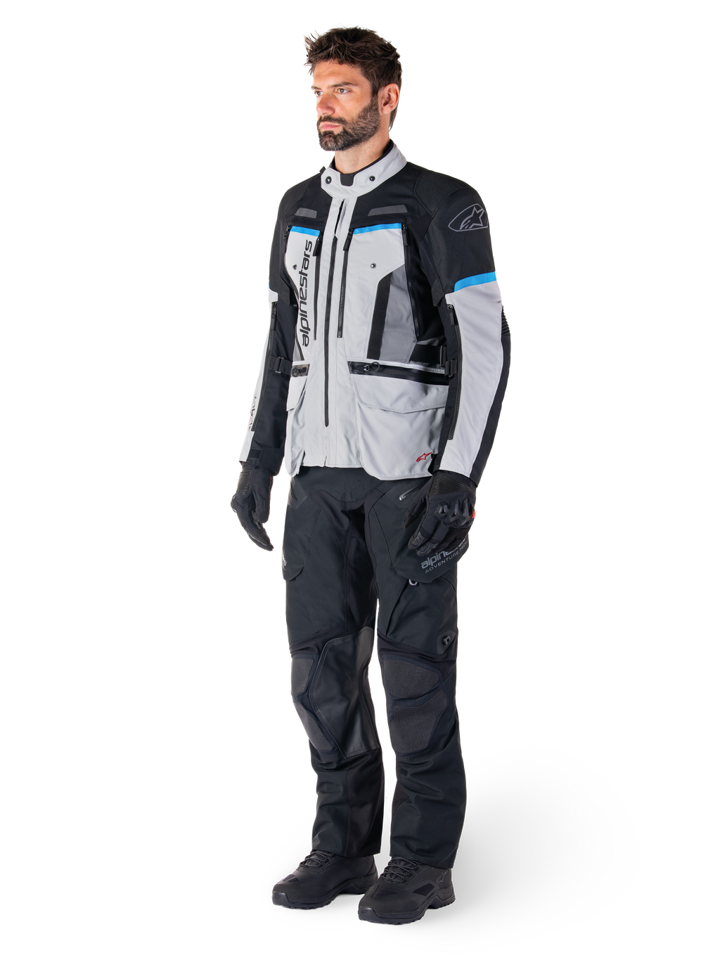 Male rider wearing Alpinestars Bogotá Pro Drystar® Jacket in Ice Gray, Black, and Cyan, paired with black technical riding pants and gloves, adventure touring gear for all-weather performance.