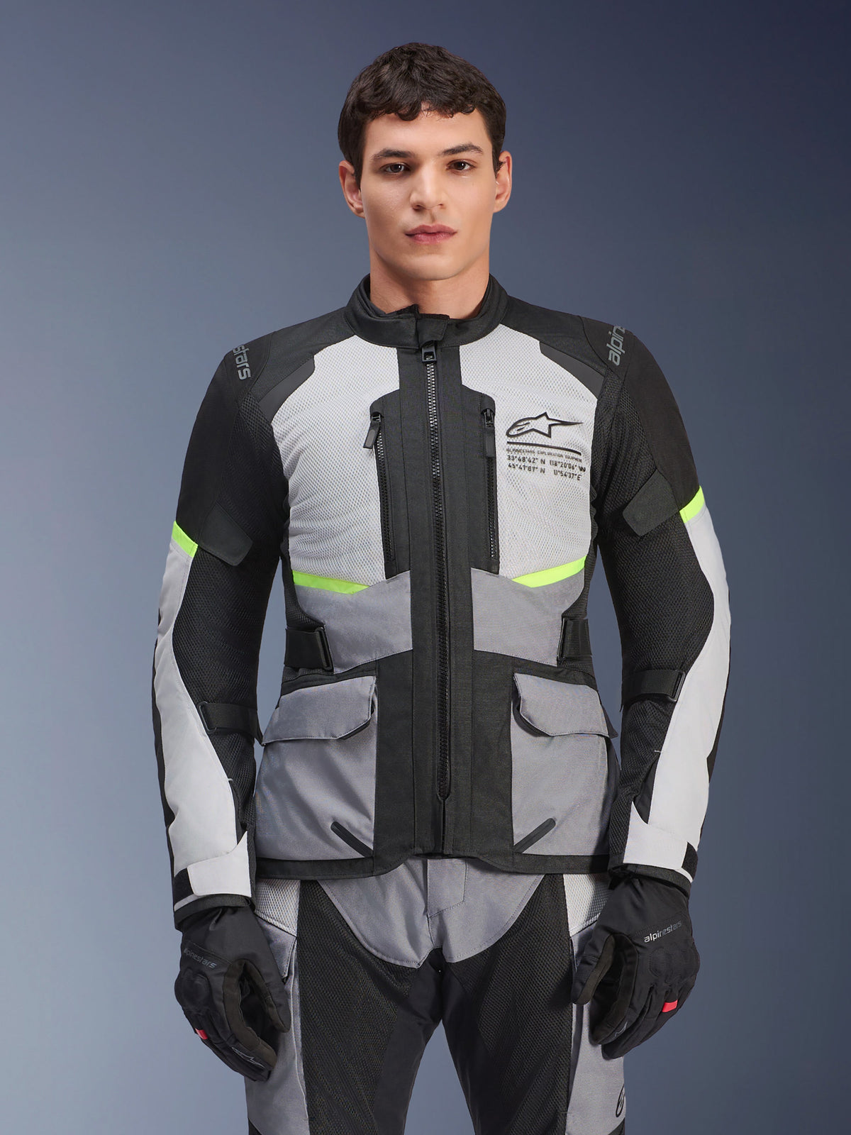 Male rider wearing Alpinestars Andes Air Drystar® Jacket in Ice Gray, Dark Gray, and Black, featuring neon yellow accents and mesh ventilation panels, styled with matching motorcycle pants and gloves, adventure touring gear