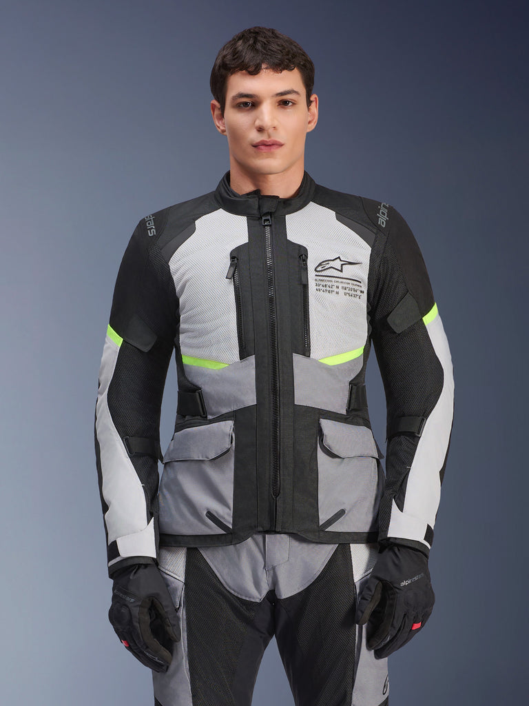 Male rider wearing Alpinestars Andes Air Drystar® Jacket in Ice Gray, Dark Gray, and Black, featuring neon yellow accents and mesh ventilation panels, styled with matching motorcycle pants and gloves, adventure touring gear