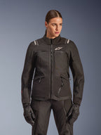 Alpinestars Stella Andes V4 Drystar Jacket, Women's Motorcycle Touring Jacket, Black, worn by a model with matching riding pants and gloves, featuring front zip closure, white logo on chest, and Alpinestars branding on the shoulders, sleek all-weather gear.