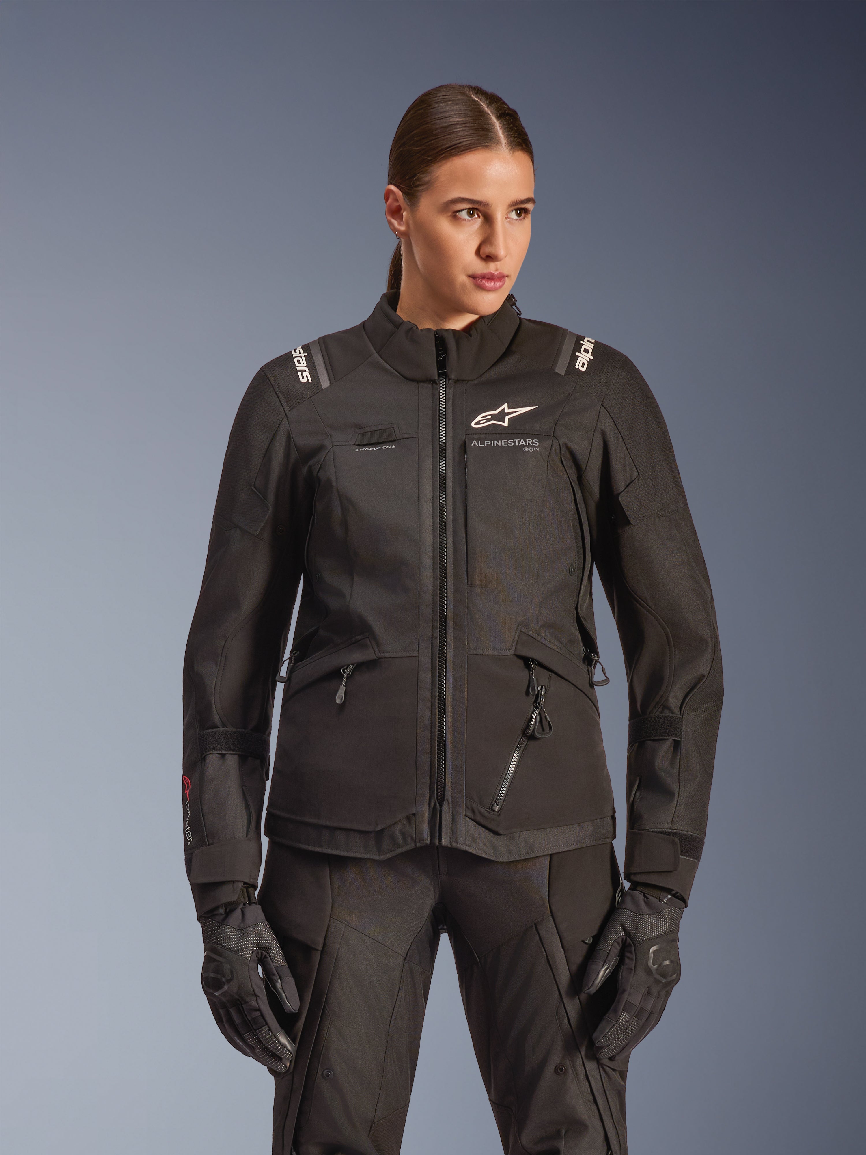Alpinestars Stella Andes V4 Drystar Jacket, Women's Motorcycle Touring Jacket, Black, worn by a model with matching riding pants and gloves, featuring front zip closure, white logo on chest, and Alpinestars branding on the shoulders, sleek all-weather gear.
