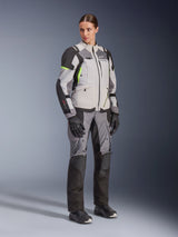 Woman wearing Alpinestars Stella Andes V4 Drystar® Jacket and matching pants, Ice Gray and Dark Gray with Yellow Fluo accents, complete adventure touring gear set with black gloves and boots, full-length studio shot.