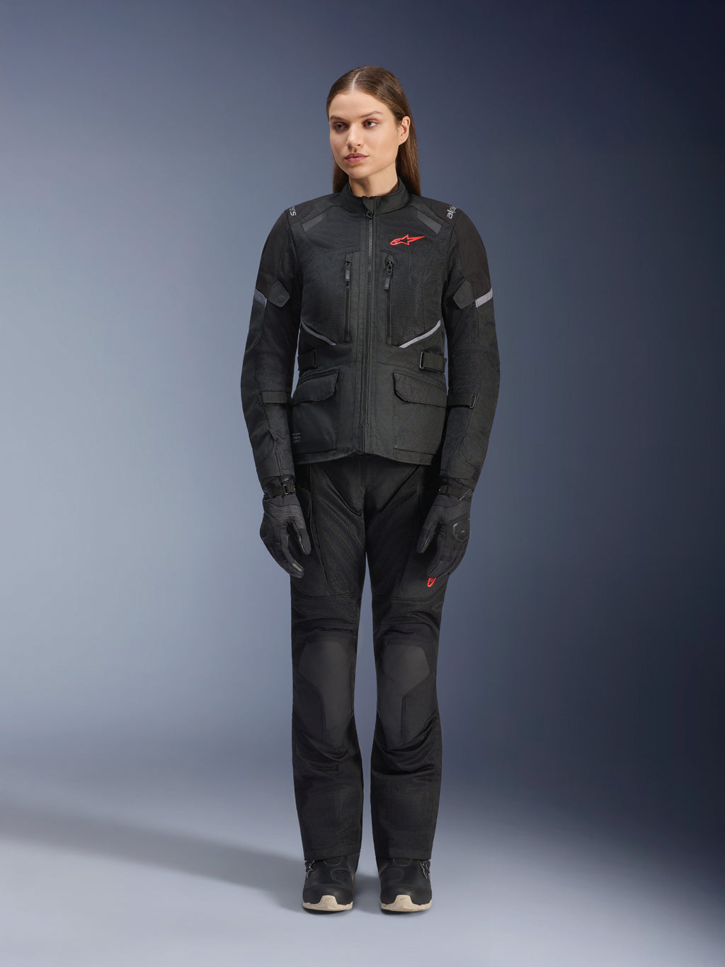 Female model wearing the Alpinestars Stella Andes Air Drystar® Jacket in Black, paired with matching black touring pants and gloves, featuring large mesh ventilation panels, red logo accents, and reflective details, professional studio shot for women's motorcycle gear.
