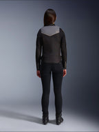 Rear view of a female rider wearing the Alpinestars Stella T-Dyno WR Jacket in Black, Dark Gray, and Ecru, paired with black slim-fit pants and black motorcycle boots, highlighting the gray upper back panel with Alpinestars logo and ecru trim details.
