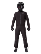 Motorcycle rider wearing Alpinestars AMT-8 Stretch Drystar® XF Pant Liner and matching jacket, all-black waterproof and windproof technical gear, featuring a black helmet, gloves, and boots, sleek adventure touring design.