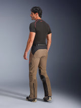 Alpinestars AMT-8 Stretch Drystar® XF Pants in Walnut Black, adventure-touring motorcycle pants shown from a back three-quarter view, featuring walnut tan textile with black panels on the seat and inner legs, accordion stretch calf panels, and AMT branding on the side, worn with a black base layer.