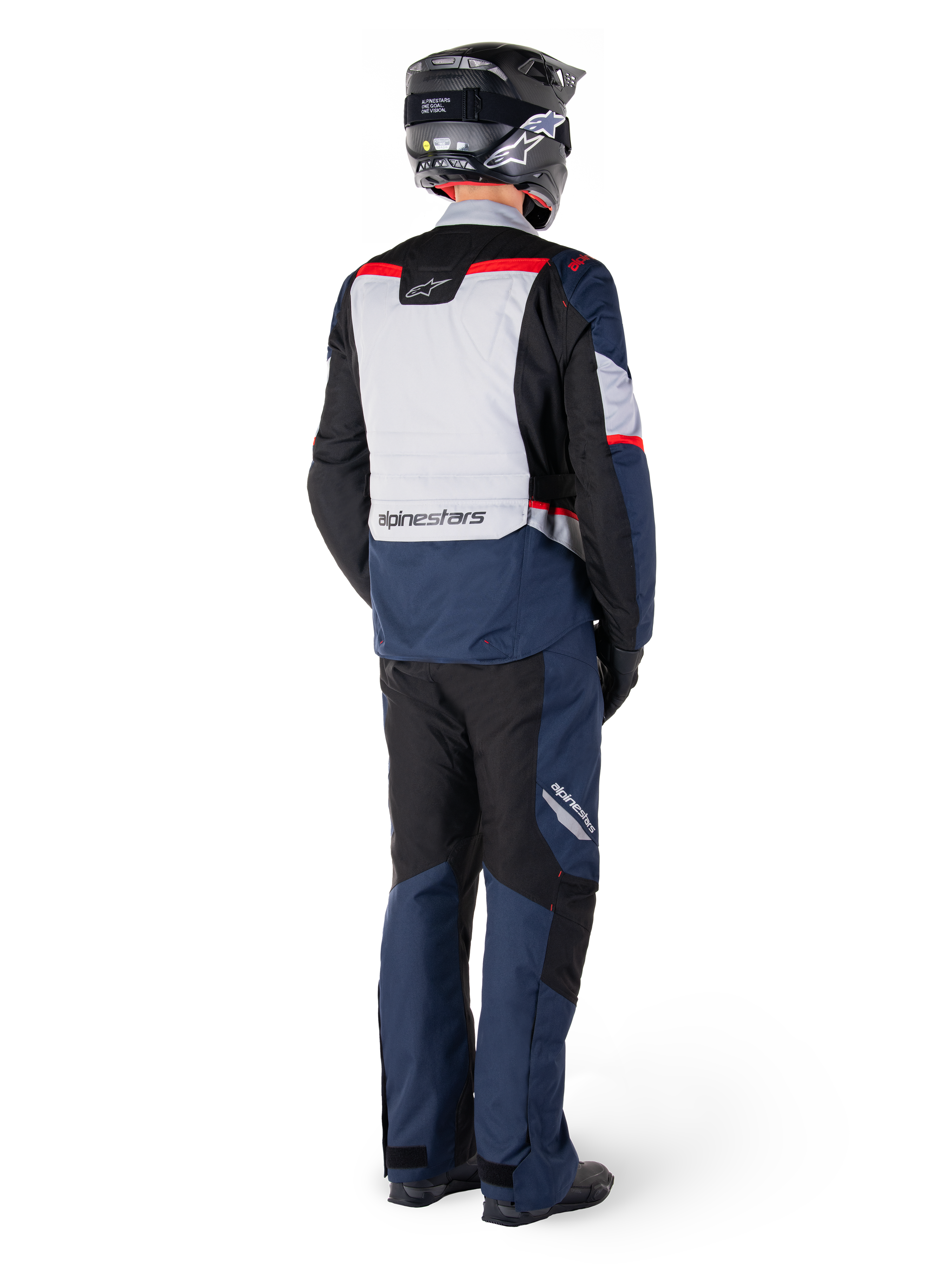 Rear view of a motorcycle rider wearing Alpinestars ST-1 Waterproof Pants and matching jacket in Dark Blue Black and Bright Red, adventure touring gear with textile panels and reflective accents, paired with a black helmet and boots.