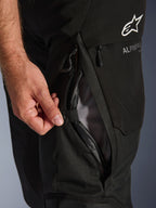Alpinestars Andes V4 Drystar® Pants, Black, close-up of the thigh ventilation system being opened by a hand to show the mesh interior, durable textile construction with Alpinestars logo and branding