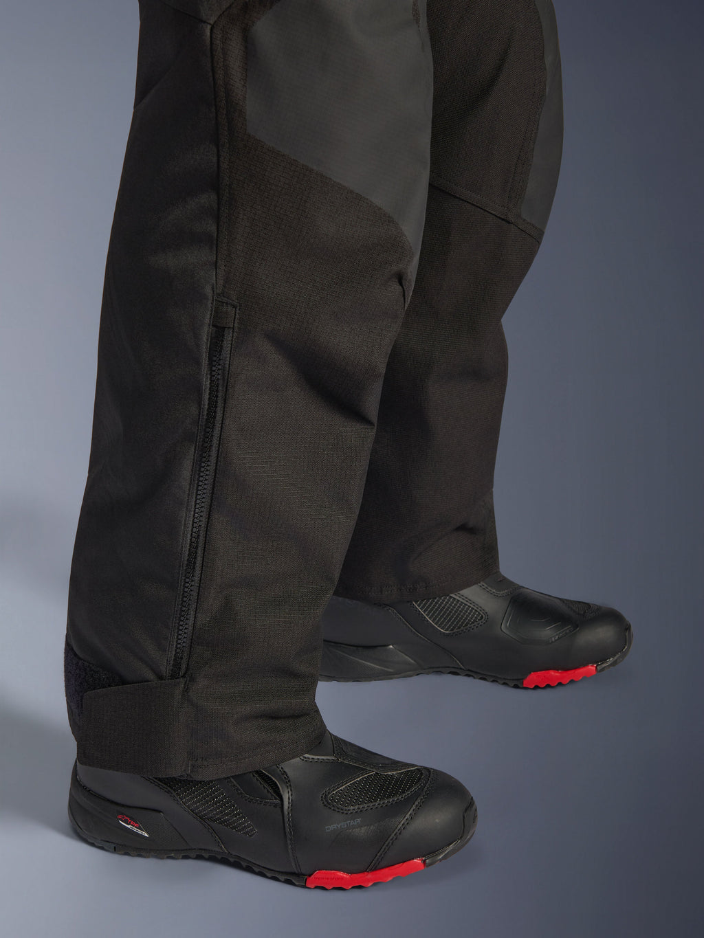 Alpinestars Andes V4 Drystar® Pants - Long, Black motorcycle adventure pants, close-up of lower leg showing adjustable zipper cuff and durable textile construction, worn with black motorcycle boots with red accents