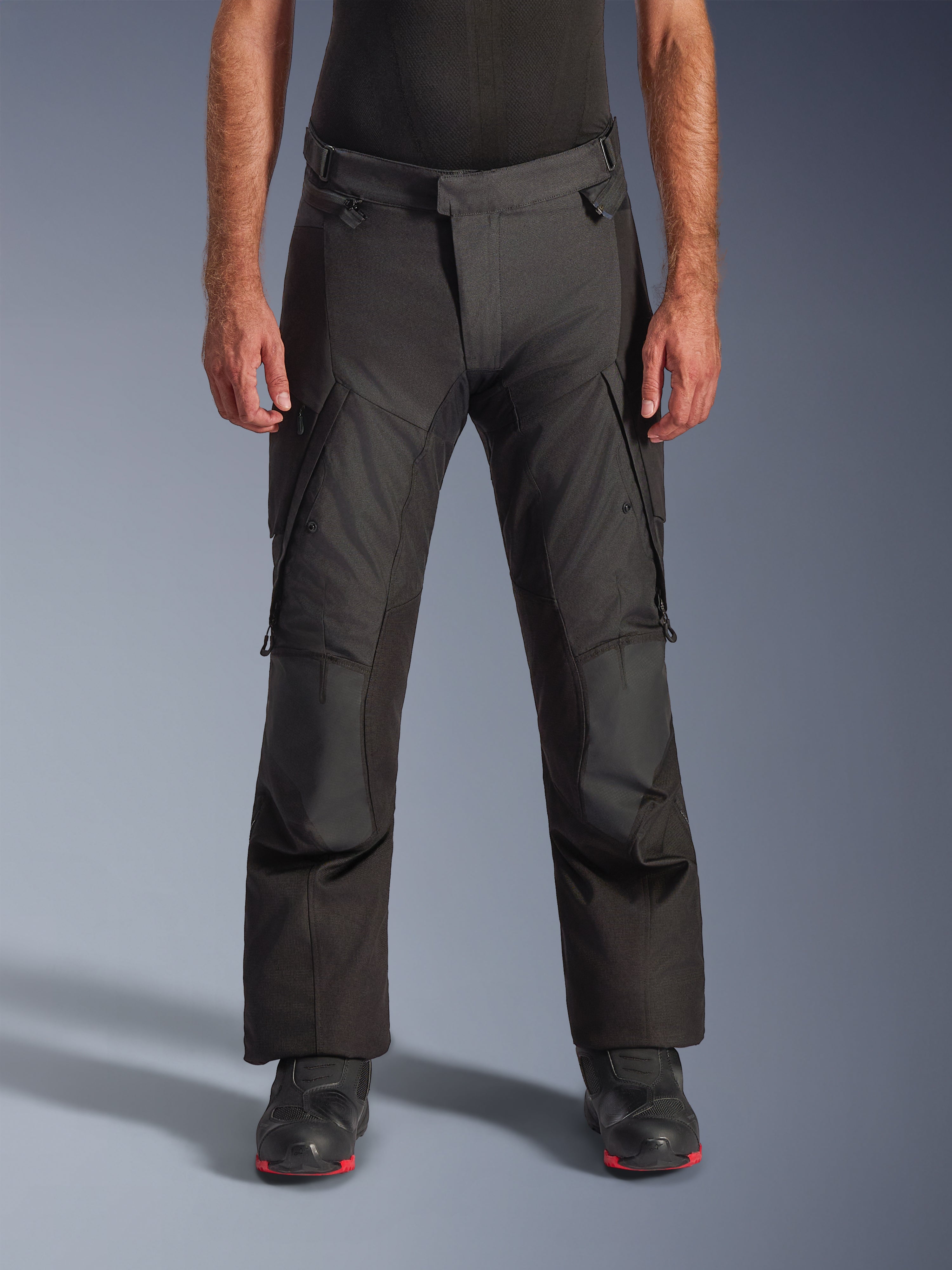 Alpinestars Andes V4 Drystar Pants, Motorcycle Adventure Touring Pants, Black with gray panels, featuring reinforced knee patches and thigh cargo pockets, worn with black riding boots, waterproof textile construction for all-weather riding