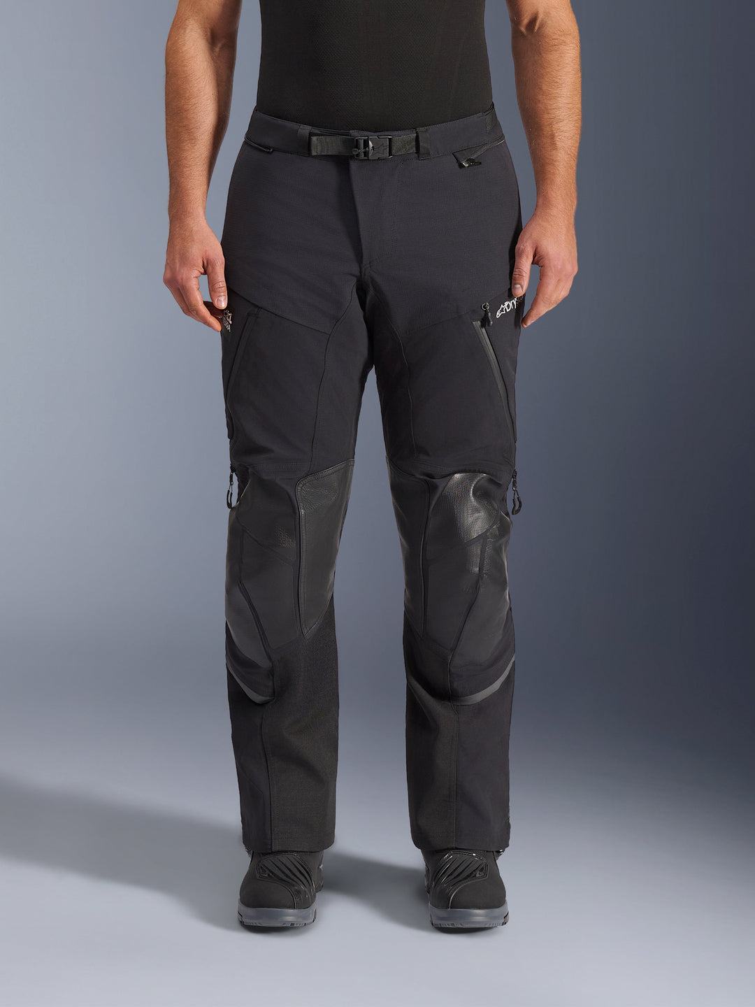 Alpinestars Andes Pro Drystar® XF Pants, Black Dark Gray adventure touring motorcycle pants, front view, featuring 3-layer laminated construction, integrated knee armor panels, waterproof zippered pockets, and magnetic waist buckle, styled with black riding boots.