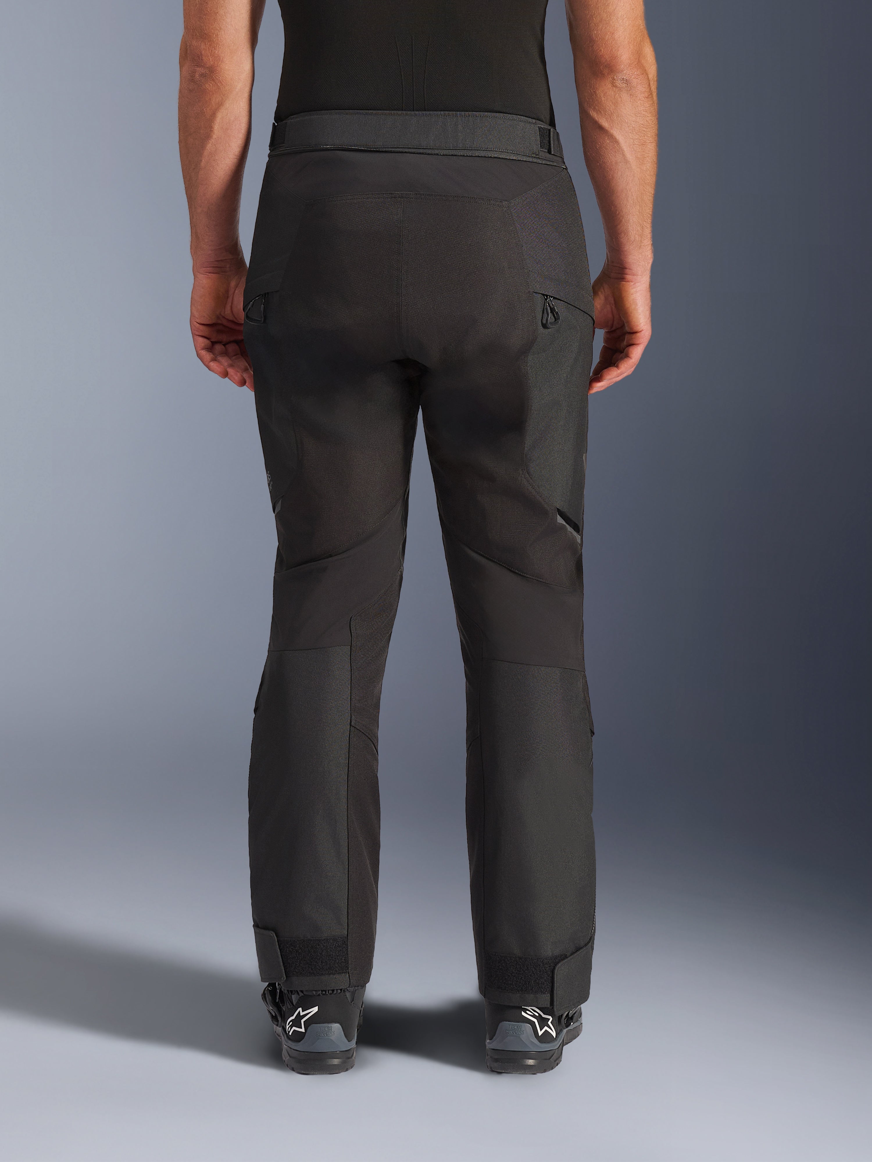 Alpinestars Cusco Drystar® Pants, Motorcycle Pants, Black, rear view worn by a rider, featuring textured textile panels, zippered vents on the thighs, and adjustable ankle closures, paired with black Alpinestars boots.