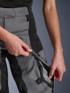 Alpinestars Woman Stella Andes V4 Drystar® Pants, Black and Dark Gray, close-up of hands opening the zippered thigh ventilation vent to reveal breathable mesh, waterproof coil zippers, durable textile construction for adventure riding