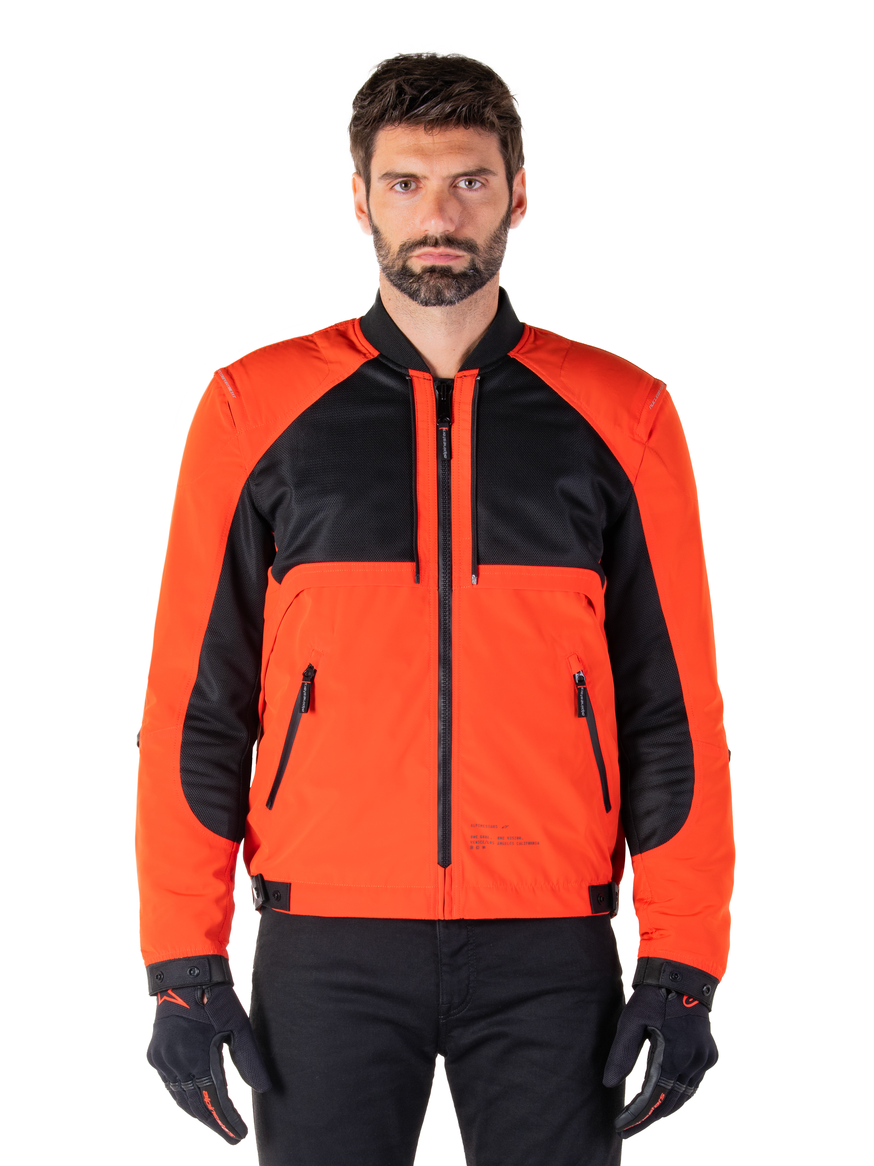 Alpinestars Mootant Waterproof Parka in Spicy Orange and Black, modular motorcycle jacket shown in a bomber-style configuration on a male model, featuring black mesh upper chest panels, bright orange torso and sleeves, front zipper, and ribbed collar, paired with black gloves and trousers