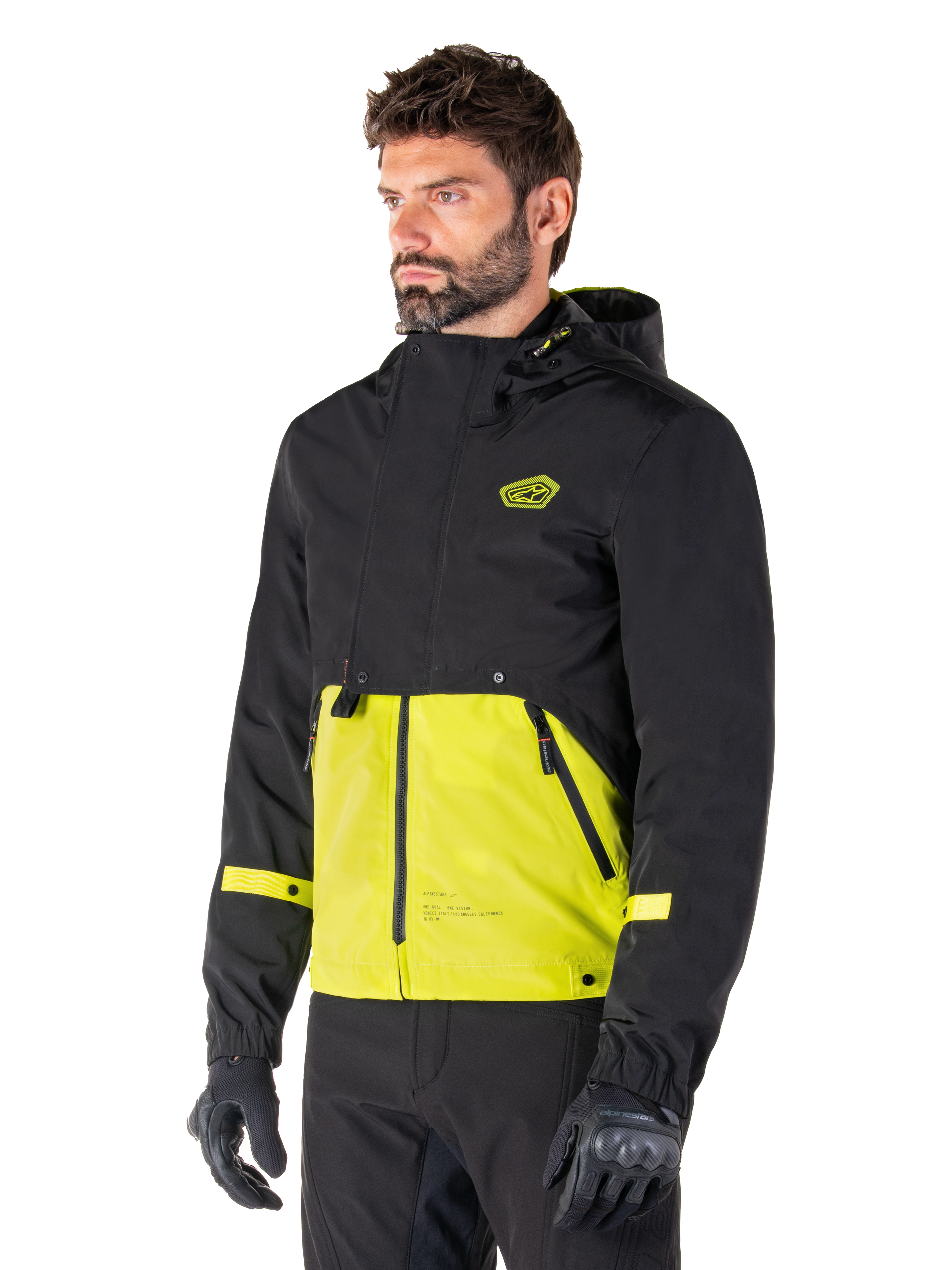 Alpinestars Mootant Waterproof Parka in Lime Punch Black, modular motorcycle jacket worn by a man with black riding gloves and pants, featuring a black upper section and sleeves with a vibrant lime green lower panel, hooded design with a utilitarian military-inspired aesthetic.