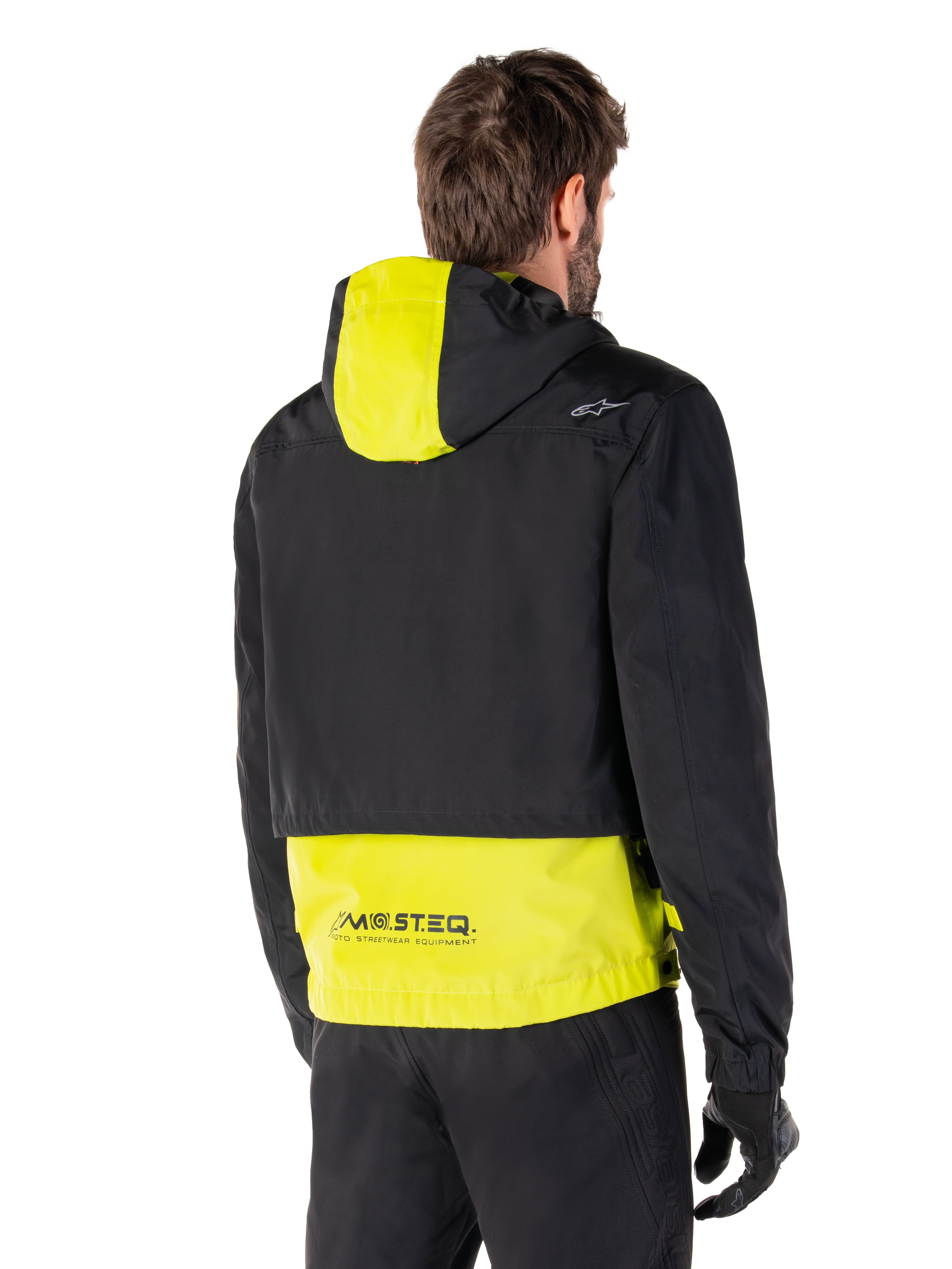 Alpinestars Mootant Waterproof Parka, Rear View, Lime Punch and Black, featuring a black upper body with a lime yellow hood panel and lower back, MO.ST.EQ. branding on the hem, worn with black riding pants and gloves, urban contemporary motorcycle jacket