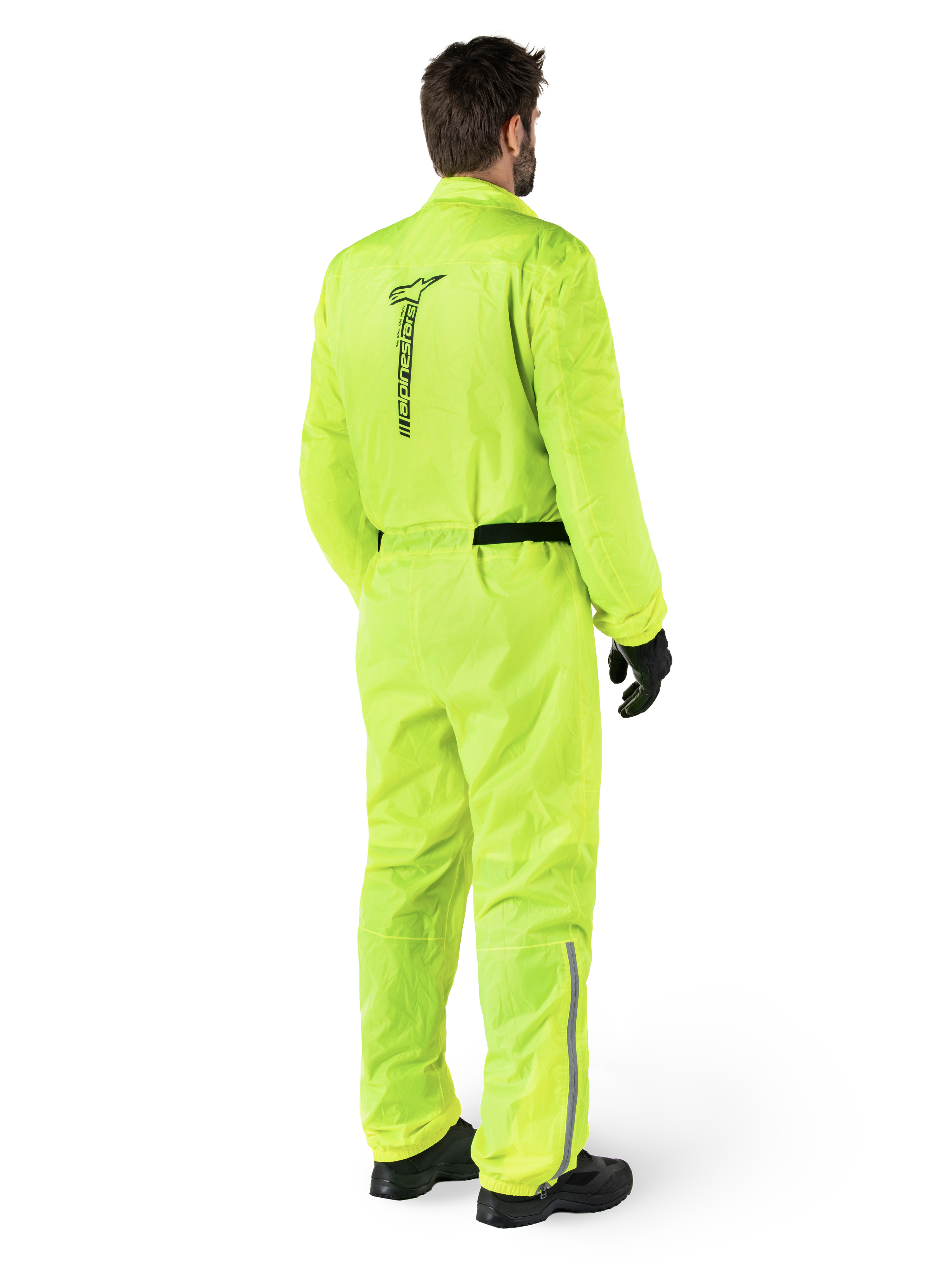 Alpinestars Hurricane Rain V2 Suit, Yellow Fluo, Rear view of a rider wearing a one-piece motorcycle rain suit, featuring a black Alpinestars logo on the back, black waist belt, and reflective strips on the lower legs, worn with black gloves and boots