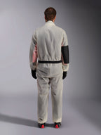 Alpinestars Kart Rain Suit, Karting Oversuit, Translucent Clear, back view showing a reinforced black panel on the right elbow for heat protection, elasticized waist with black trim, see-through material revealing a racing suit underneath, paired with black gloves and racing boots.