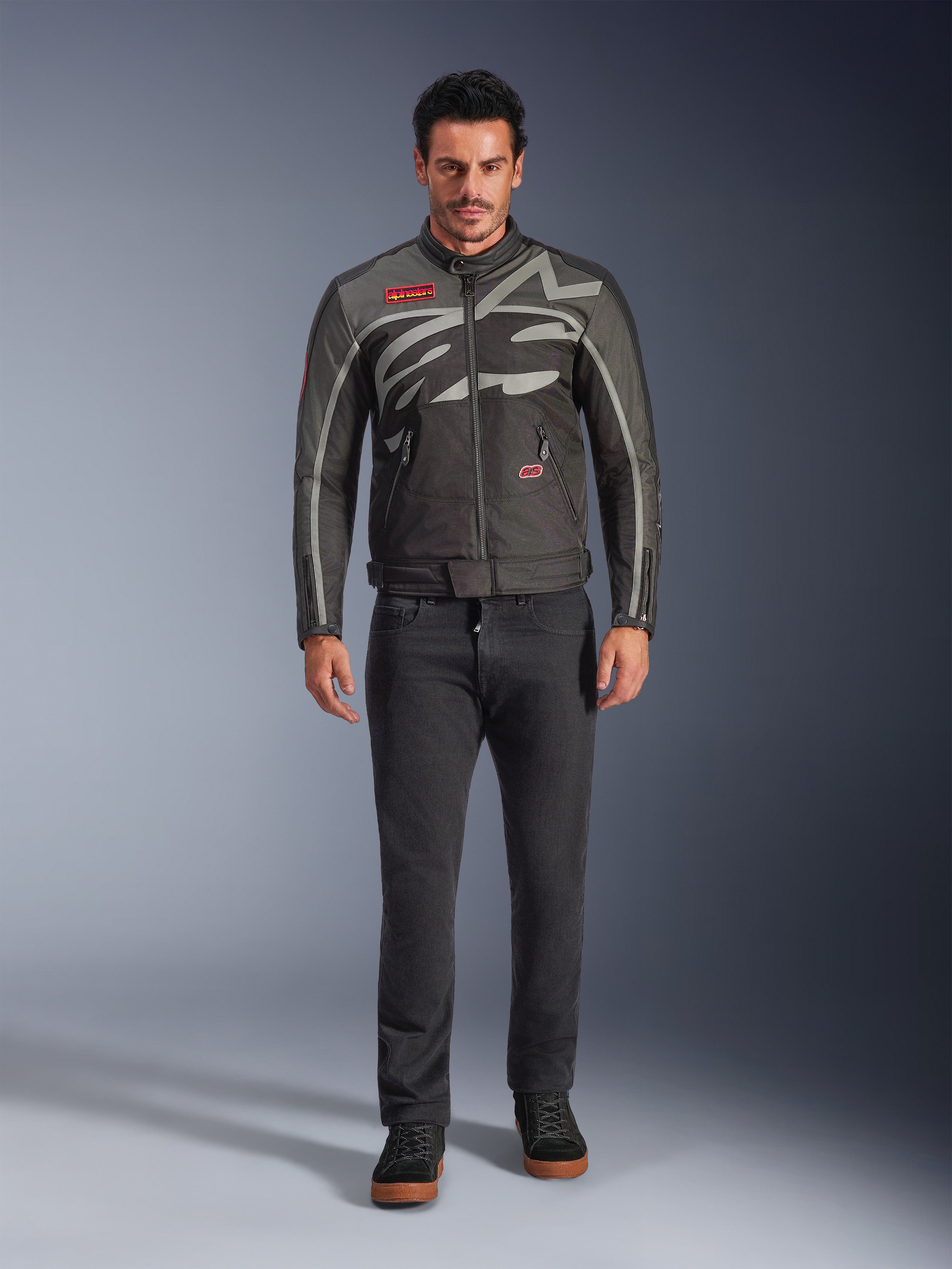 Alpinestars Axton Jacket, Motorcycle Jacket, Black Anthracite Red Tangerine, worn by a model with dark pants, featuring a wrap-around gray Alpinestars logo, red brand patches, and a water-resistant textile shell for urban road riding