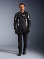 Male model wearing the Alpinestars AST V3 Air Jacket in Black with white accents, featuring mesh ventilation panels and a sporty fit, paired with black technical riding pants, gloves, and boots, front view, technical motorcycle gear for warm-weather riding.