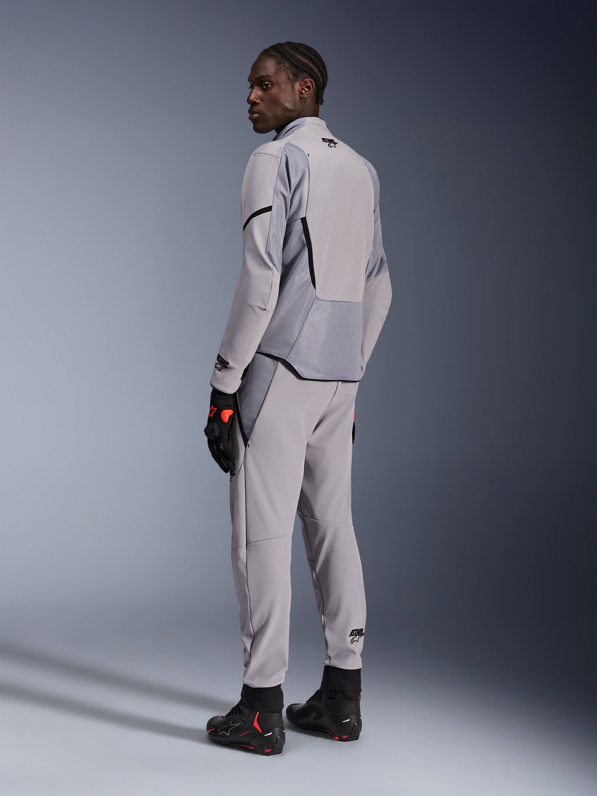 Alpinestars Aeroshell Airflow Jacket in Mid Gray Anthracite, worn with matching pants and black racing gloves, back view showing laser-perforated panels and athletic sport fit, professional motorcycle apparel
