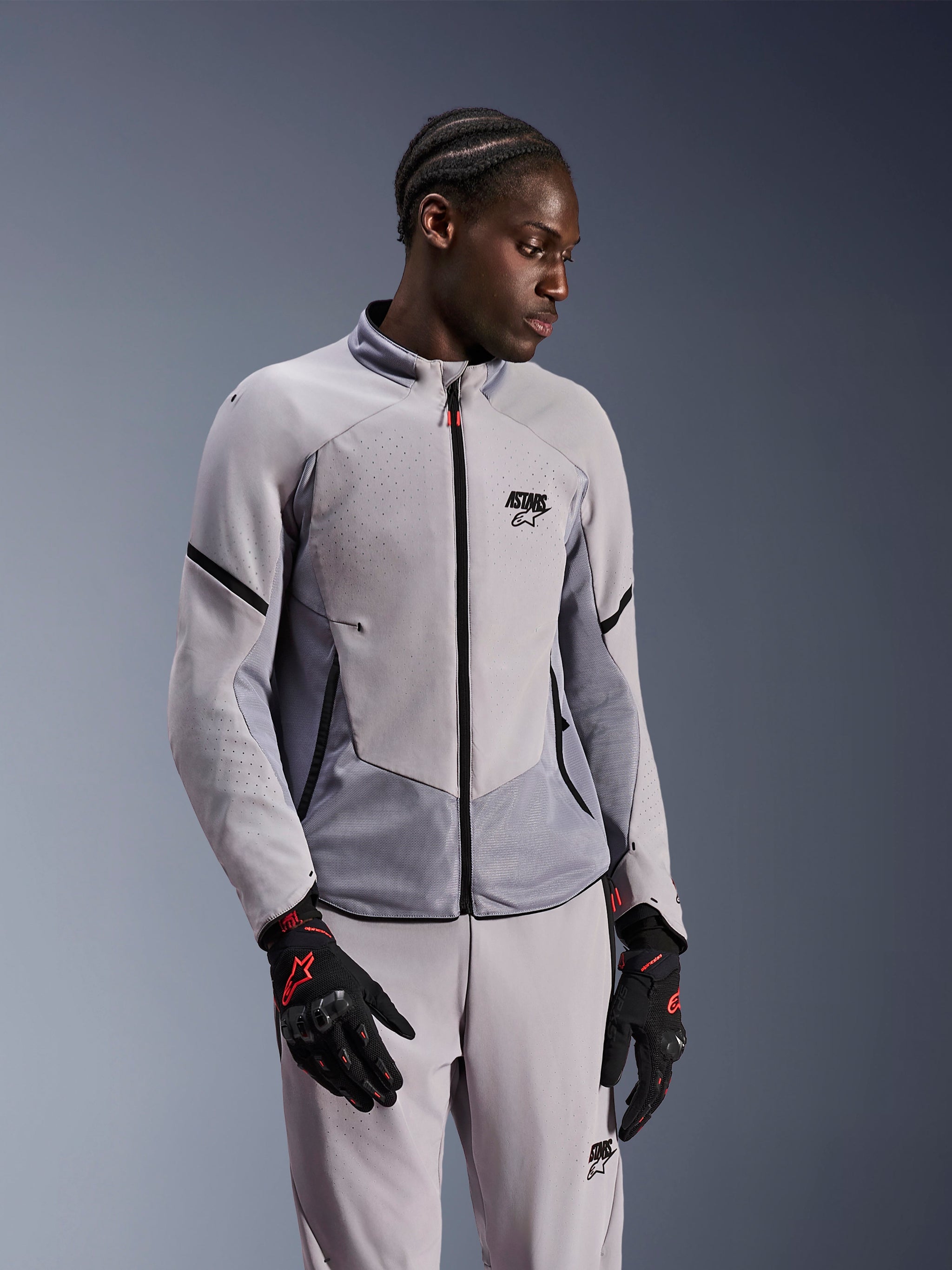 Alpinestars Aeroshell Airflow Jacket, Mid Gray Anthracite, worn by a model with matching textile pants and black gloves with red accents, featuring laser-perforated zones and mesh panels for ventilation, sleek sport-fit design for motorcycle riding.