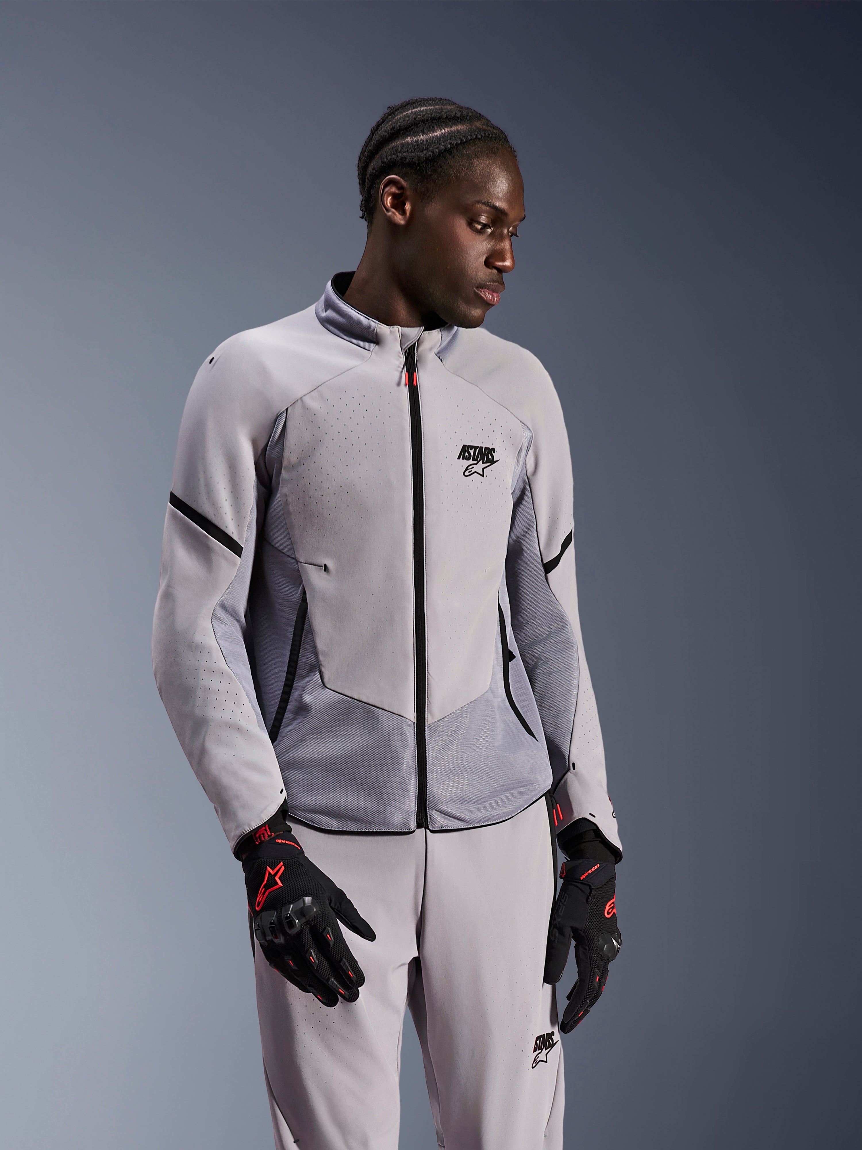 Alpinestars Aeroshell Airflow Jacket, Mid Gray Anthracite, worn by a model with matching textile pants and black gloves with red accents, featuring laser-perforated zones and mesh panels for ventilation, sleek sport-fit design for motorcycle riding.