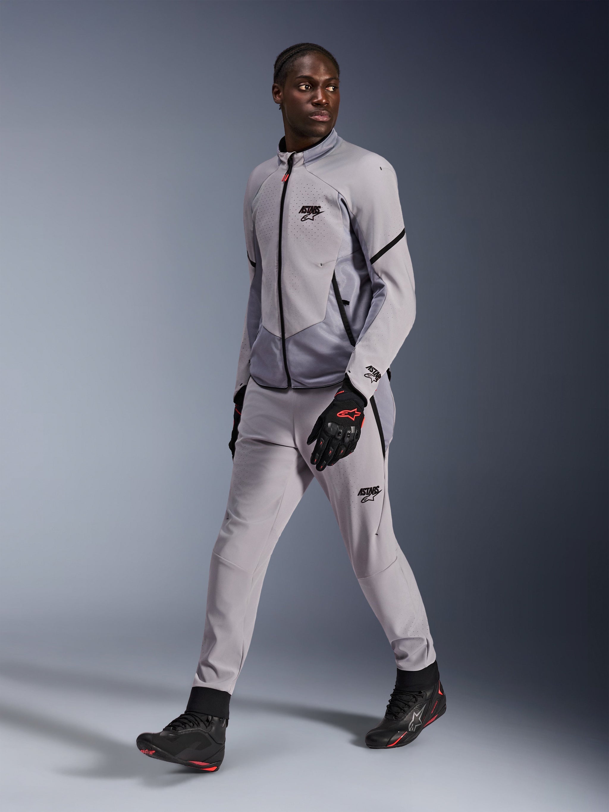 Alpinestars Aeroshell Airflow Jacket in Mid Gray Anthracite, worn by a male model with matching gray riding pants and black gloves, featuring laser-perforated chest ventilation and a sleek sport-cut design.