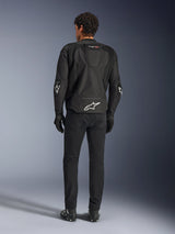 Alpinestars T-GP Air Jacket, Black, rear view on model, showing 3D mesh ventilation panels and aerodynamic hump, featuring white star logo on lower back and elbows, worn with black motorcycle pants and gloves, sport riding apparel.