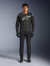 Alpinestars T-GP Air Jacket, Black textile motorcycle jacket with a large white Astars logo on the chest, worn by a model with black riding pants and gloves, featuring perforated panels and mesh ventilation for sport riding