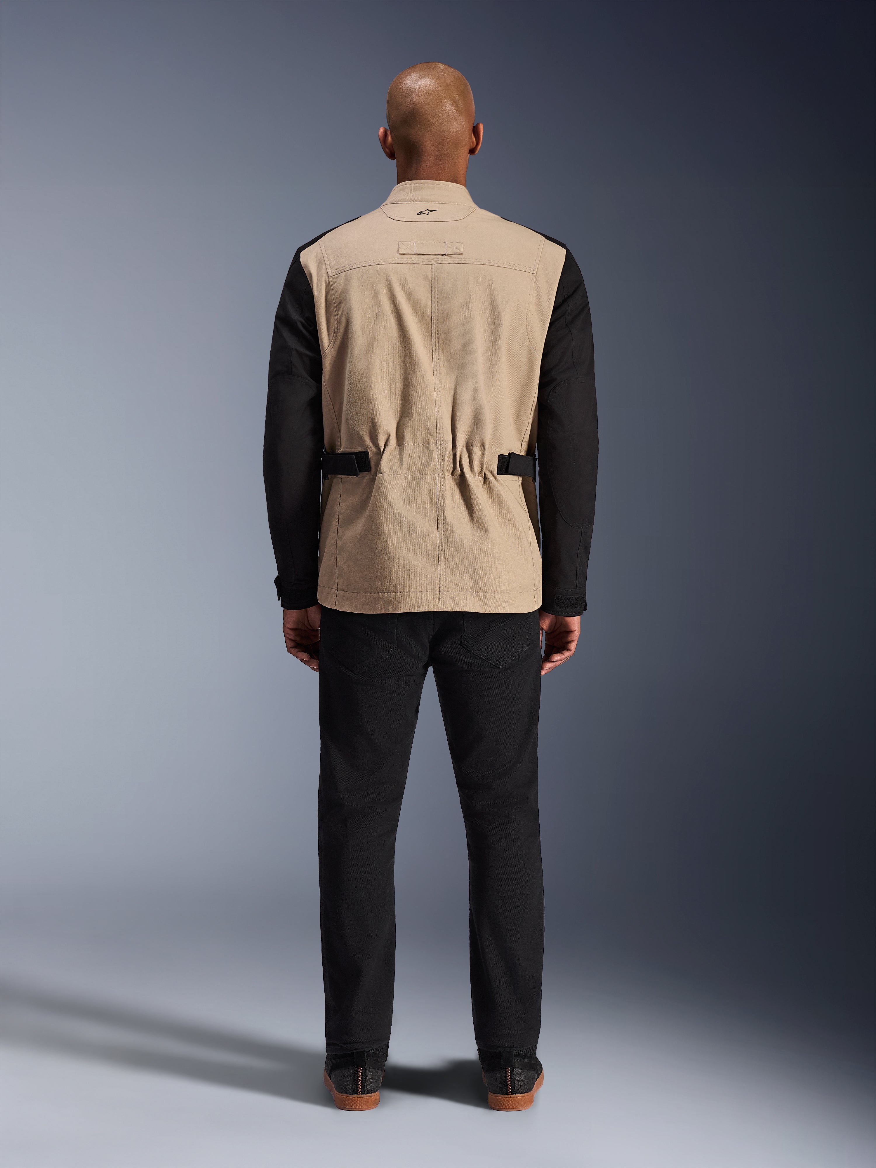 Alpinestars Dice Jacket, Urban Motorcycle Jacket, Tan and Black, Rear view on model, featuring polycotton twill construction, adjustable waist straps, and small embroidered logo on the collar, worn with black pants