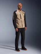 Alpinestars Dice Jacket, Urban Motorcycle Jacket, Aluminum Black and Tan, two-tone design with black sleeves and a khaki torso, worn by a model with black pants and black sneakers, workwear-inspired aesthetic with utility pockets and embroidered branding on the sleeve.