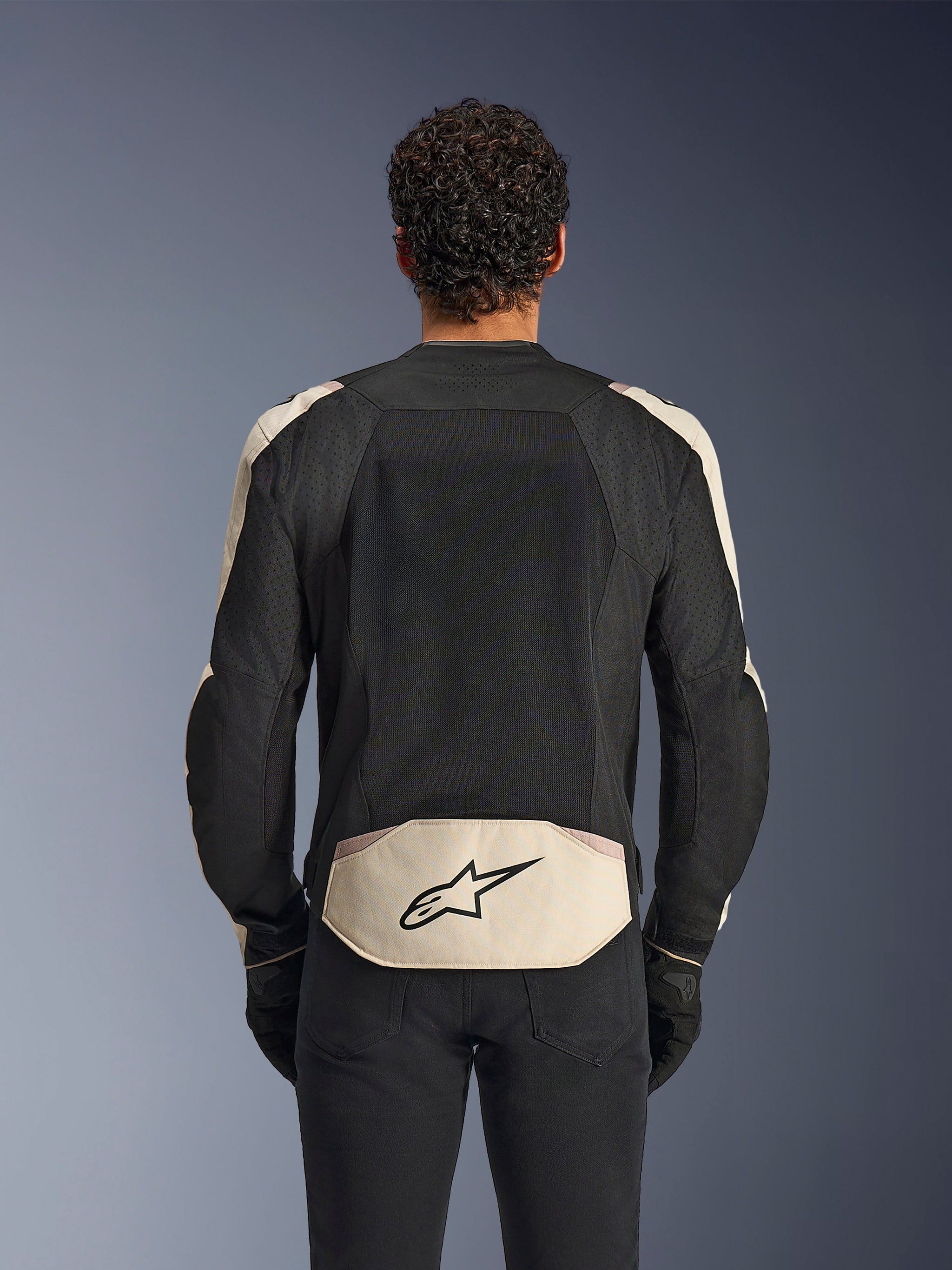 Alpinestars T-SPS Air V2 Jacket in Black Mastic Aluminum, back view, featuring a large mesh back panel for ventilation, light-colored panels on the shoulders and lower back with the Alpinestars logo, worn with black riding pants and gloves.