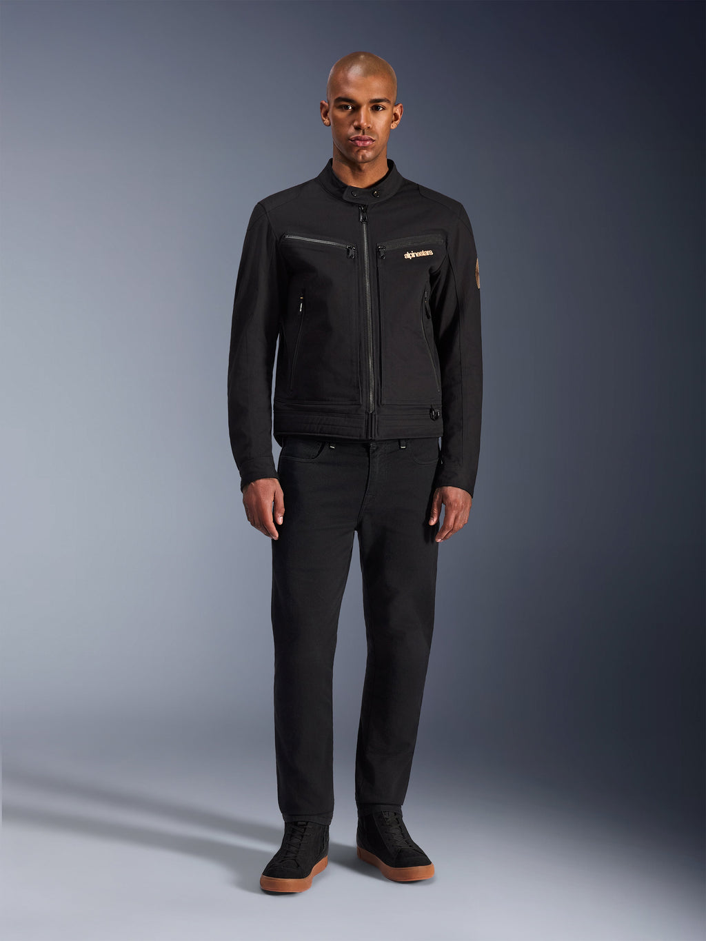 Alpinestars Bruiser Jacket, Black urban motorcycle jacket, worn by model with black pants and high-top sneakers, front view showing zippered chest pockets and embroidered logo, classic workwear-inspired design for everyday commuting