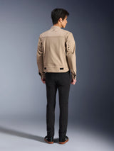Rear view of a model wearing the Alpinestars Bruiser Jacket in brown, an urban motorcycle jacket with workwear-inspired design, featuring metal eyelet details on the back and waist adjusters, paired with black pants and sneakers, contemporary street riding style.