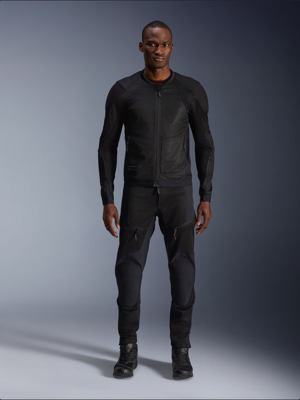 Male model wearing the Alpinestars Troop-Air Jacket in Black Black, lightweight mesh motorcycle jacket, paired with matching black riding pants and boots, featuring a technical 2D tech mesh construction for superior airflow.