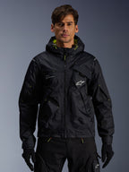 Alpinestars Mogress Air Jacket, urban motorcycle jacket, Black with Lime Punch accents, worn by a model with black riding pants and gloves, utility-inspired design with a hood and white star logo on the chest, lightweight textile gear for street riding