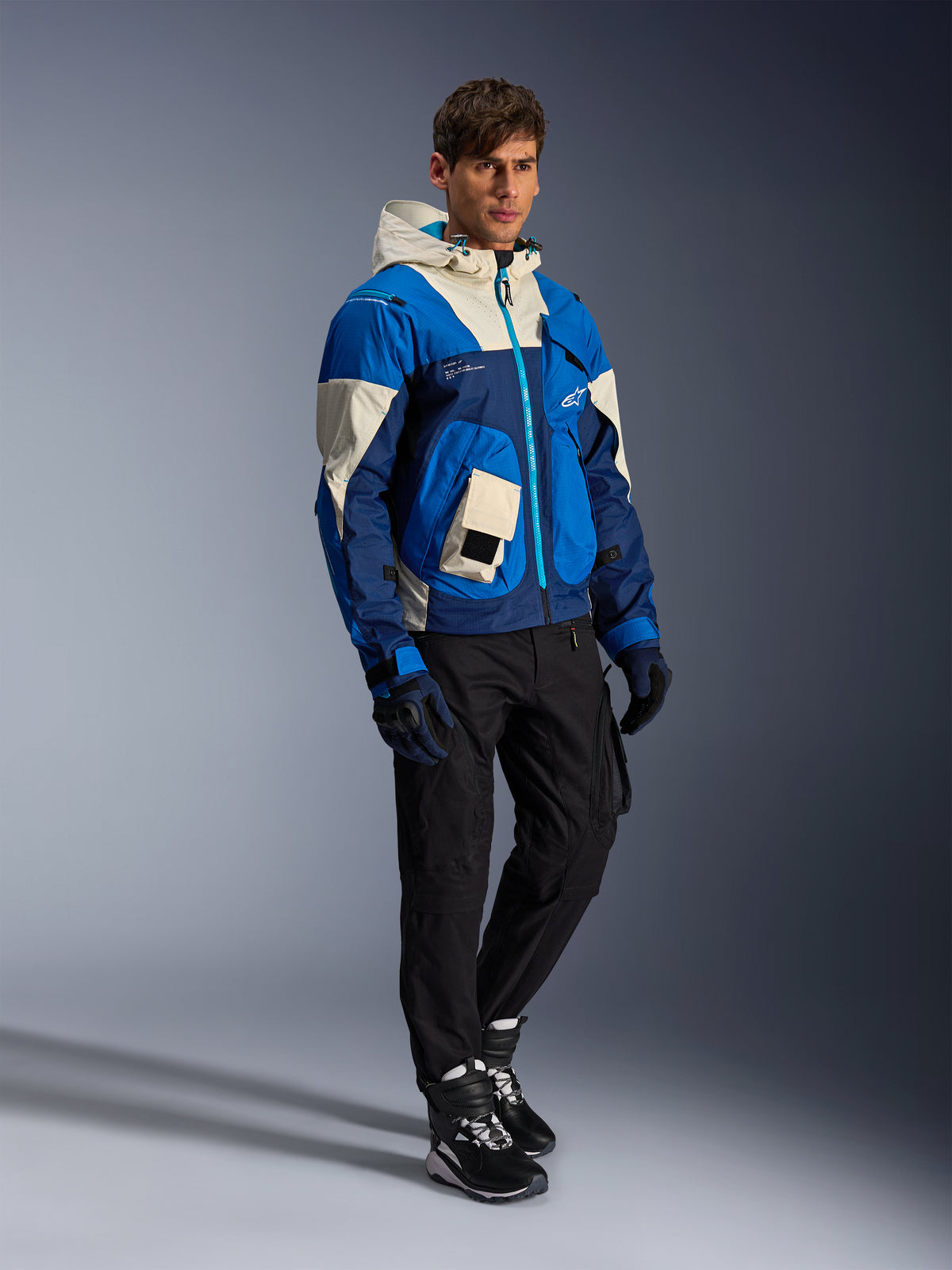 Alpinestars Mogress Air Jacket, Urban Motorcycle Jacket, Blue Almond with cream and navy panels, featuring a hood and utility pockets, worn with black riding pants, gloves, and boots, contemporary streetwear-inspired protective gear.