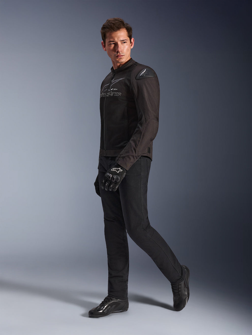 Alpinestars SMX Air Jacket in Black Anthracite, worn by model with matching black riding pants, gloves, and shoes, studio full-body shot, performance sport motorcycle gear featuring tech mesh and shoulder sliders