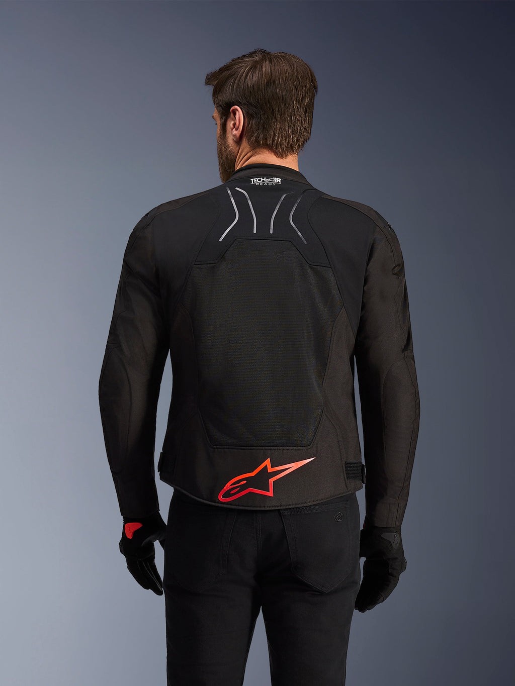 Alpinestars SMX Air Jacket, Rear View, Black with Bright Red Alpinestars logo on the lower back, featuring a high-airflow tech mesh panel and Tech-Air Ready branding, worn by a male rider with black pants and gloves